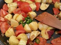 2 - Dans un grand plat de cuisson (style plat à paella, wok ou tajine), faire revenir les merguez dans un peu d'huile d'olive jusqu'à légère coloration. Retirer et réserver. Dans le même plat faire suer l'oignon et l'ail 2 à 3 mn, rajouter les tomates, mélanger et laisser cuire quelques minutes, puis rajouter les pommes de terre, mélanger. Incorporer successivement, l'harissa, le ras el hanout, le paprika, le curcuma, le concentré de tomates, le piment vert et le persil (ou la coriandre - en réserver un peu pour la présentation), saler et poivrer.