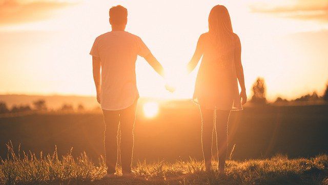 couple debout se tenant la main et regardant le coucher de soleil