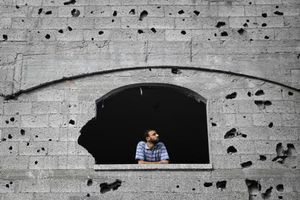 A Palestinian man looks through a window scarred with shrapnel