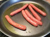 2 - Dans un grand plat de cuisson (style plat à paella, wok ou tajine), faire revenir les merguez dans un peu d'huile d'olive jusqu'à légère coloration. Retirer et réserver. Dans le même plat faire suer l'oignon et l'ail 2 à 3 mn, rajouter les tomates, mélanger et laisser cuire quelques minutes, puis rajouter les pommes de terre, mélanger. Incorporer successivement, l'harissa, le ras el hanout, le paprika, le curcuma, le concentré de tomates, le piment vert et le persil (ou la coriandre - en réserver un peu pour la présentation), saler et poivrer.