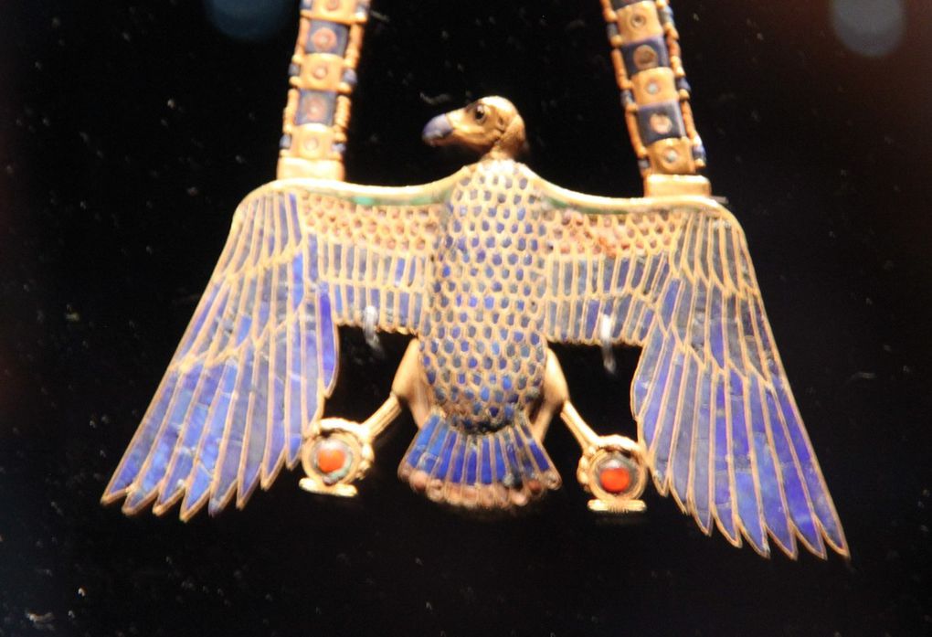  L'image d'Horus, le dieu primordial du ciel est reproduite sur ce pendentif d'une grande finesse d'exécution.     Le plumage de l'oiseau est réalisé en turquoise, cornaline, lapis-lazuli et  en pâte de verre bleue.     Sa tête est surmontée d'un disque flamboyant et il tient dans ses serres  les hiéroglyphes ank ( vie) et chen ( infinité, les attibuts idéaux du soleil  éternel et vivifiant. 