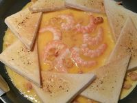 3 - Ressortir du four les tranches de pain de mie dorées. Verser un filet d'huile d'olive dans une poêle, laisser chauffer, puis disposer les triangles de pain de mie en rosace et les faisant se chevaucher. Verser l'omelette au centre de la poêle, laisser prendre quelques instants, puis réduire la puissance sur feu doux (5-6), incorporer les différents ingrédients (crevettes et chorizo) et laisser cuire 5 à 8 mn selon la consistance que vous aimez (baveuse ou non).   