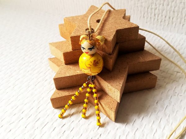 La petite kokeshi prénommée Hikari est montée sur un collier en cordon de coton écru de 56 cm de tour de cou. La poupée mesure 2.5 cm et est agrémentée de perles de rocaille jaune et dorée