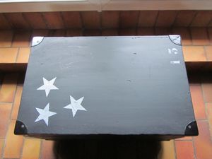 N°13 -Ancienne caisse militaire, avec poignées sur les côtés, coins métalliques et ajout de 4 roulettes en dessous, peinte en noire, vernie en acrylique mat, trois etoiles et nombre 13 peints sur le couvercle. 45 x 72 x 45 cm.