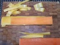 1 - Laver et éplucher les carottes. Les tailler en fines bandes de largeur identique. Couper les bords bien droits pour un beau rendu.  Les placer à plat l'une sur l'autre en les décalant comme sur la photo (la bande du dessous doit être un peu plus longue que l'autre). Les enrouler sur elles-mêmes, les redresser et les maintenir en rouleau avec une pique en bois.