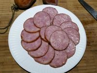 3 - Peler et écraser la gousse d'ail avec le plat d'un couteau. Faire revenir l'ail dans une poêle avec le beurre, rajouter le chou égoutté et laisser étuver à couvert, puis incorporer la moitié de la sauce à la crème, rectifier l'assaisonnement si besoin . Remettre le four à préchauffer th 6 (180°). Découper les pommes de terre en rondelles de 2 à 3 mm d'épaisseur, tailler la saucisse en rondelles de la même façon. Remettre le cercle autour de la pâte, étaler une couche de chou en tassant un peu, ôter le cercle et disposer les rondelles de saucisse, puis celles de pommes de terre au centre. Enfourner le tout pour 10 mn environ th 6 (180°). Déguster dès la sortie du four en rajoutant un peu de sauce au centre de la tarte fine pour un bel effet visuel.