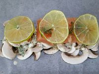 3 - Couper le 1/2 citron vert en fines rondelles. Recouvrir une plaque allant au four d'un grand rectangle de papier sulfurisé, disposer au centre les champignons émincés, puis arroser avec la préparation de sauce. Couper le pavé de saumon en 4 et placer les morceaux par dessus, poivrer, saler et saupoudrer de piment d'Espelette. Venir ajouter un peu d'aneth, et terminer par les rondelles de citron vert. Refermer les papillotes (voir technique de pliage dans l'article "Papillotes de gambas p-d-terre au beurre d'herbes") et enfourner à th 7 pour 15 à 18 mn. 