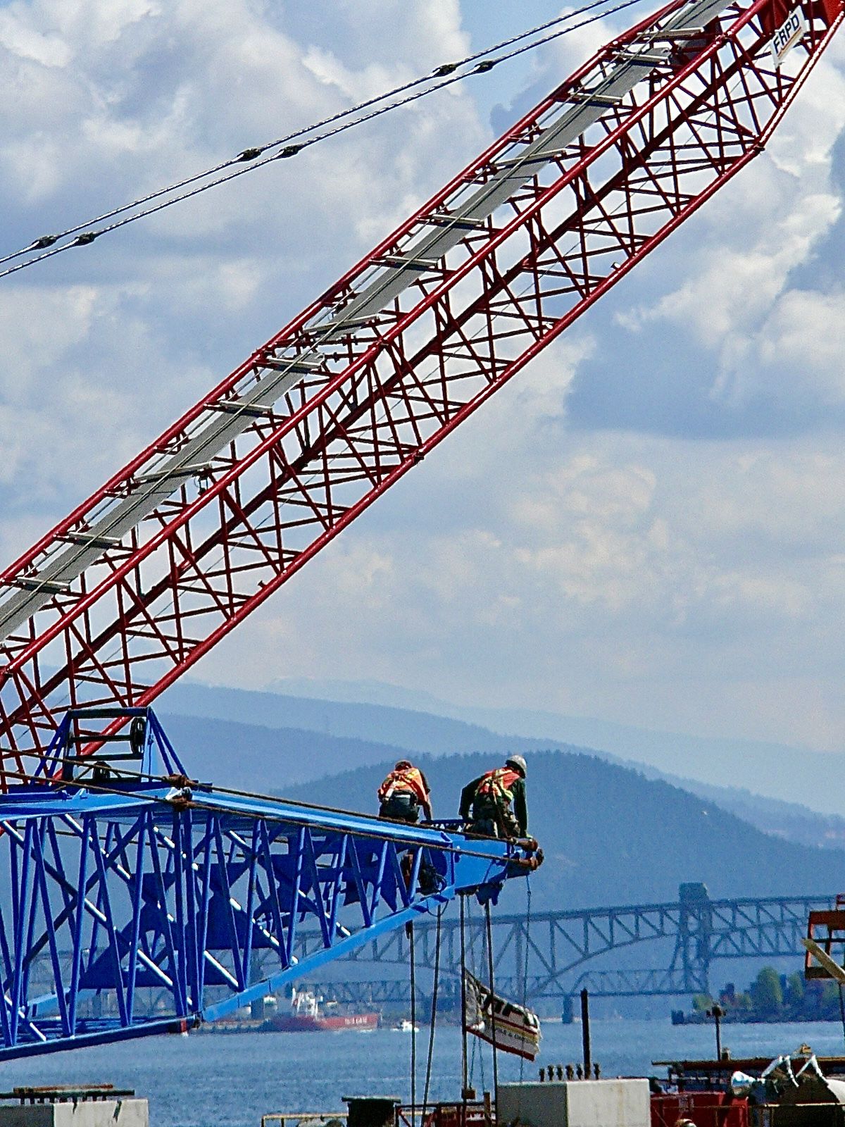 Deux personnes travaillant sur des grues de couleurs bleue et rouge au dessus de l’eau