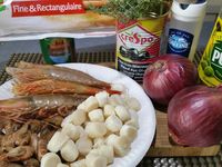 1 - Faire cuire les gambas dans une casserole d'eau bouillante salée. Peler les oignons et les émincer. Egoutter et réserver les gambas cuites. Faire revenir rapidement (1 à 2 mn) les noix de pétoncles dans une poêle avec de l'huile d'olive. Couper les olives noires dénoyautées en rondelles. Faire revenir les oignons dans une poêle avec un bon filet d'huile d'olive jusqu'à ce qu'il deviennent translucides. Mettre votre four à préchauffer th 6 (180°).  Etaler la pâte feuilletée sur un plat allant au four et la badigeonner légèrement d'huile d'olive avec un pinceau, puis piquer la pâte à la fourchette.