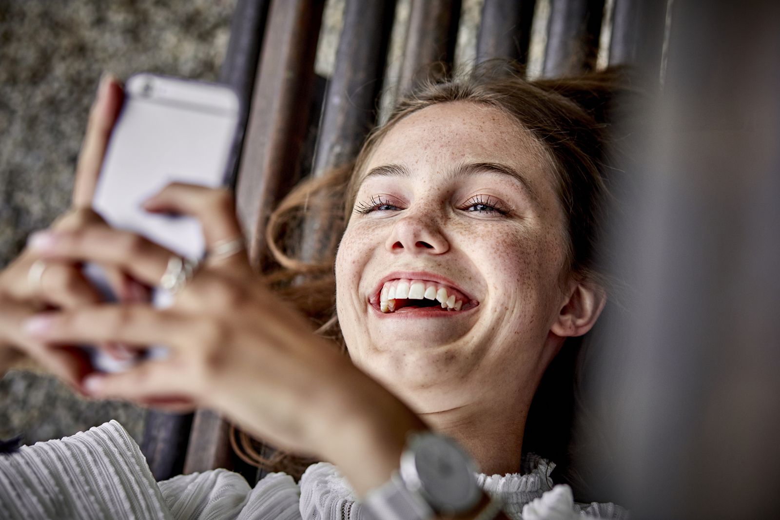 femme souriante allongée sur un banc telephone à la main