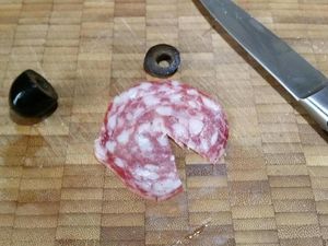 2 - Découper avec un emporte-pièce rond de 10 cm environ un disque dans le blanc de dinde. Réserver. Réaliser une entaille en triangle dans une autre tranche de saucisson, oter le bout ouvert d'un olive noire dénoyautée d'1/3, rouler la tranche de saucisson en cône et l'insérer dans l'olive. Découper un nouveau disque plus petit de blanc de dinde avec un emporte-pièce de 5 cm environ.