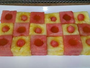 2 - Disposer la composition sur une jolie assiette à dessert. Verser dans les cavités des cubes de pastèque le coulis de mangue (ou de fruits rouges selon vos préférences). Réserver au frais. Ciseler quelques feuilles de verveine fraîche.