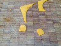 2 - Découper une forme en coeur dans du papier sulfurisé, reporter ce gabarit sur la tranche de mimolette et découper. Dans la 2ème tranche de poulet réaliser un disque avec un emporte-pièce rond qui servira pour la tête du chien. Faire les yeux du chien dans les chutes de la tranche de mimolette. Couper une olive noire dénoyautée en fine rondelle et en petits morceaux courbes pour les yeux, la bouche puis tailler de petits éclats noirs pour les moustaches. Une rondelle de cornichon et le bout sans trou de l'olive noire serviront à réaliser la truffe. Découper dans la tomate un morceau en forme de langue, 2 bandes rectangulaires dans la 2ème tranche de poulet pour les pattes et deux demi-cercles pour les oreilles.