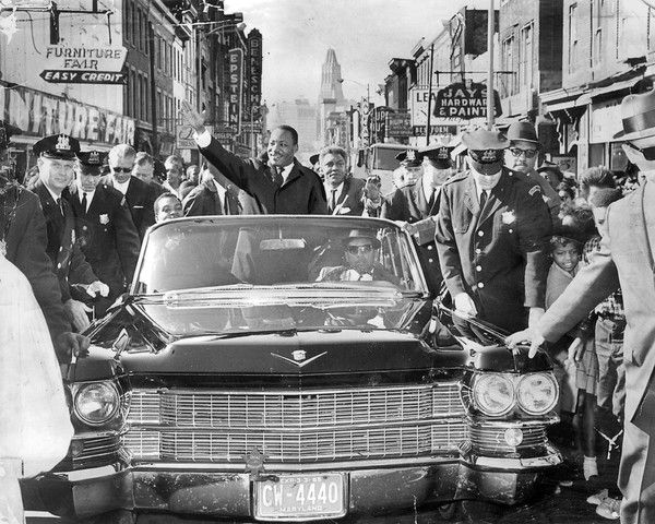 The Rev. Dr. Martin Luther King, Jr., greeting admirers on a tour up Baltimore's North Gay Street in October 1964. 