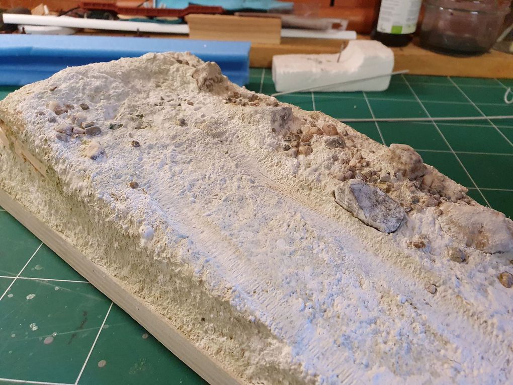 Fabrication de la base Après avoir collé un morceau de polystirène extrudé et l'avoir recouvert d'une pâte confectionné avec du carton et de la colle à placo. Après séchage, je l'ai peinte en blanc et j'ai ajouté du sable et des petits cailloux.