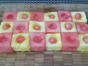 1 - Découper l'ananas et la pastèque de façon à obtenir 12 cubes de chaque très réguliers et de taille similaire. Les disposer pour former un rectangle en alternant ananas et pastèque  A l'aide d'une cuillère parisienne évider le centre de chaque cube. Placer dans les cubes d'ananas des billes de pastèque. 