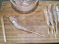 1 - Equeuter les champignons de Paris et peler les têtes. Les trancher en fines lamelles, réserver. Peler et hacher finement l'échalote. Prendre des petites piques en bois et embrocher les gambas de façon à ce qu'elles se maintiennent droites à la cuisson (ne pas ôter la carcasse avant d'embrocher les gambas).