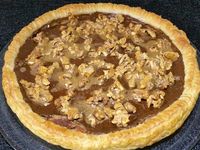 3 - Etaler la pâte feuilletée et la piquer à la fourchette. Disposer sur le fond de tarte la préparation à la noix, égaliser, puis étaler en couche la préparation à la crème de café. Enfourner la tarte pour une vingtaine de minutes environ. Pendant le temps de cuisson préparer la garniture en mélangeant dans un récipient les noix grossièrement concassées, la confiture de lait et un jaune d'oeuf. Au bout de 20 mn de cuisson, sortir la tarte du four, répartir sur le dessus la garniture aux noix concassées et enfourner à nouveau pour 7 à 8 mn environ en surveillant. La pâte doit finir de bien gonfler et dorer.