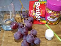 2 - Laver et sécher les raisins. Découper 2 fines rondelles dans le Chamallow. Faire un trou au centre des rondelles de chamallow avec un petit emporte-pièce rond et insérer les smarties. Positionner les chamallows à l'intérieur du verre bien collés à la paroi, et remplir le verre de grains de raisin.