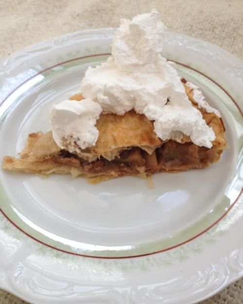 apple pie slice with cream on top on a white plate