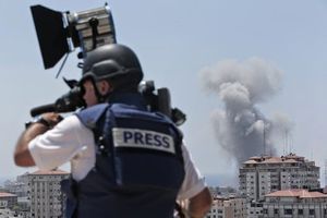 A news cameraman films at a live position as in the background smoke rises from an Israeli strike